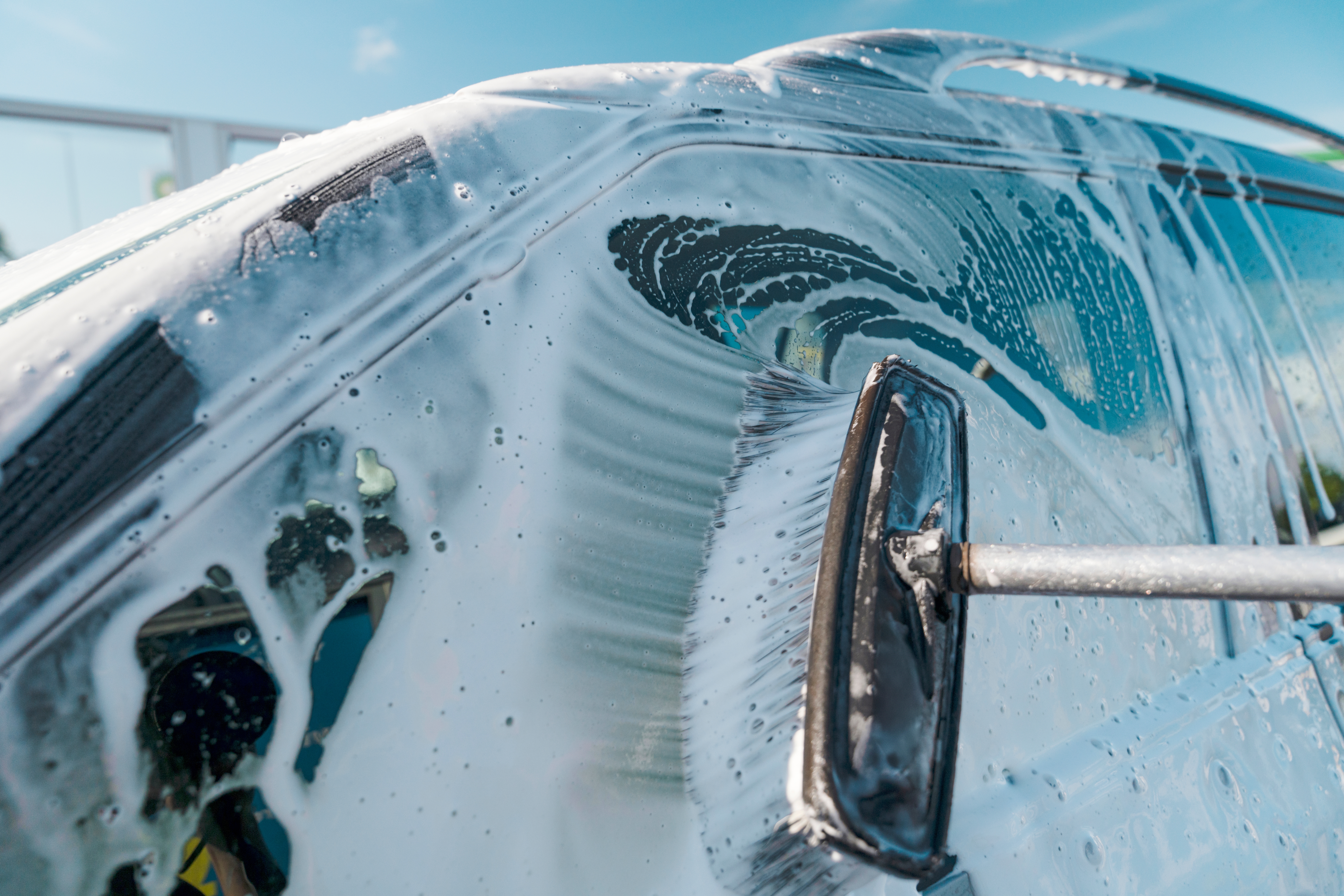 A low view of a car being washed outside using a large brush