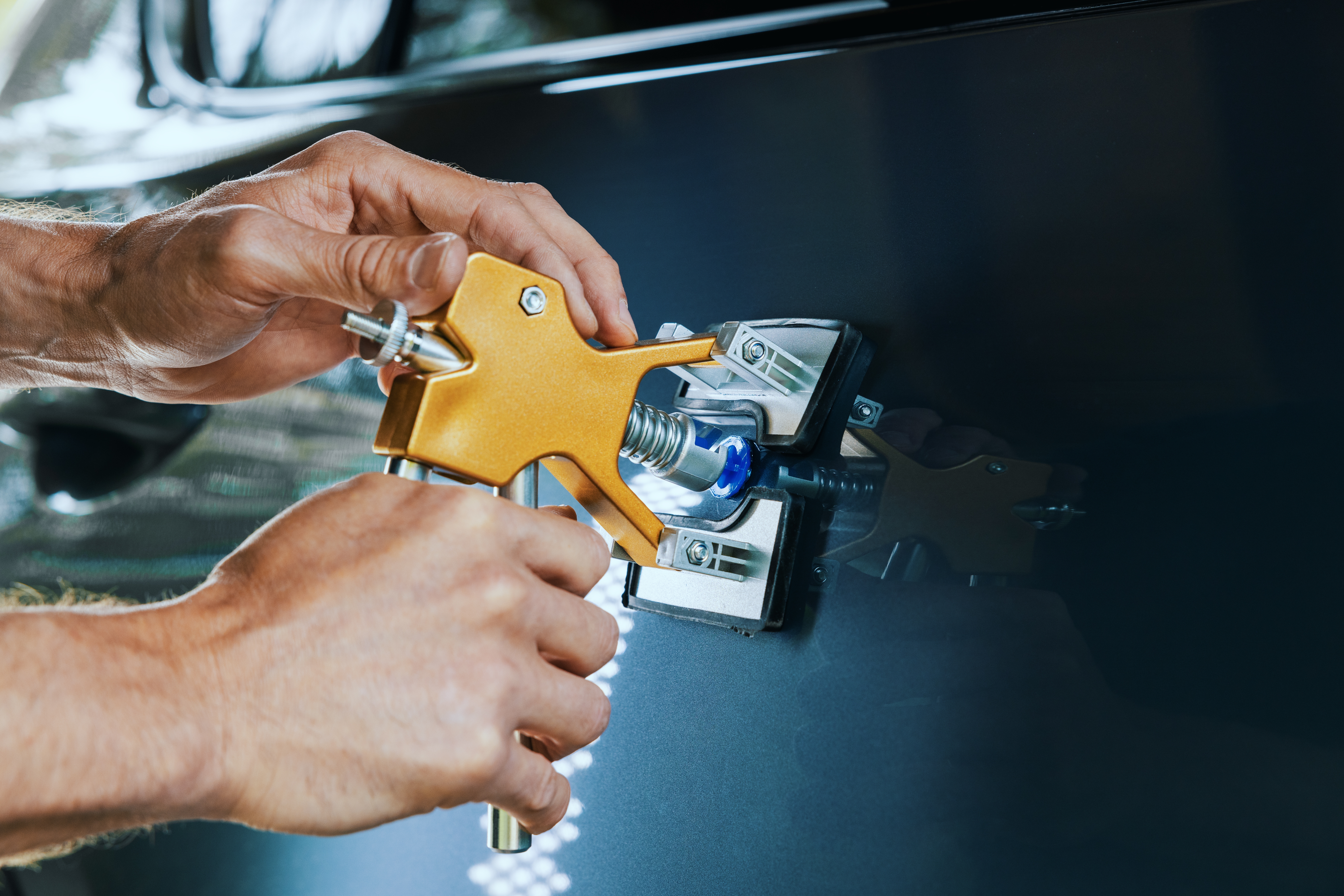 A technician using a tool for getting a dent out of a car