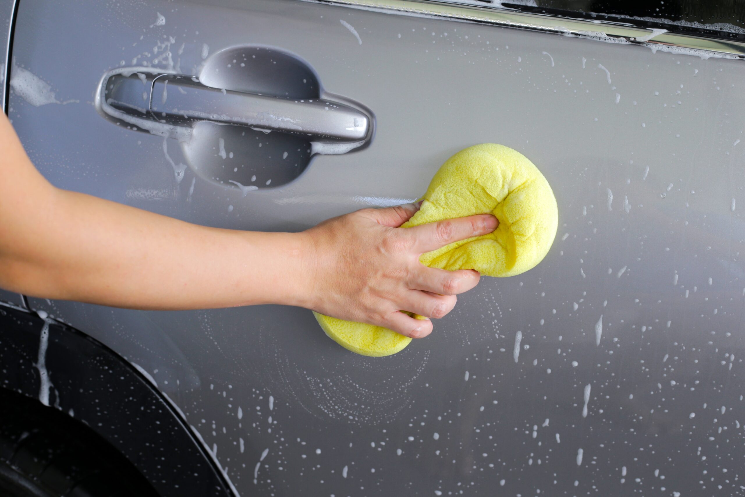 A technician wiping down a car with a sponge